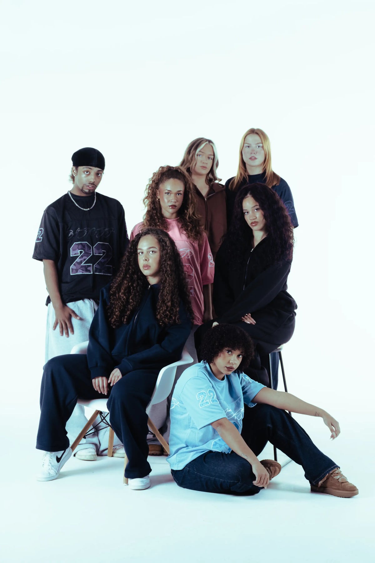Seven models showcasing the BASICSS streetwear collection, featuring 22 Camo Jerseys in black, pink and light blue, alongside oversized Cloud Tracksuits and zip-up hoodies in a minimalist studio.