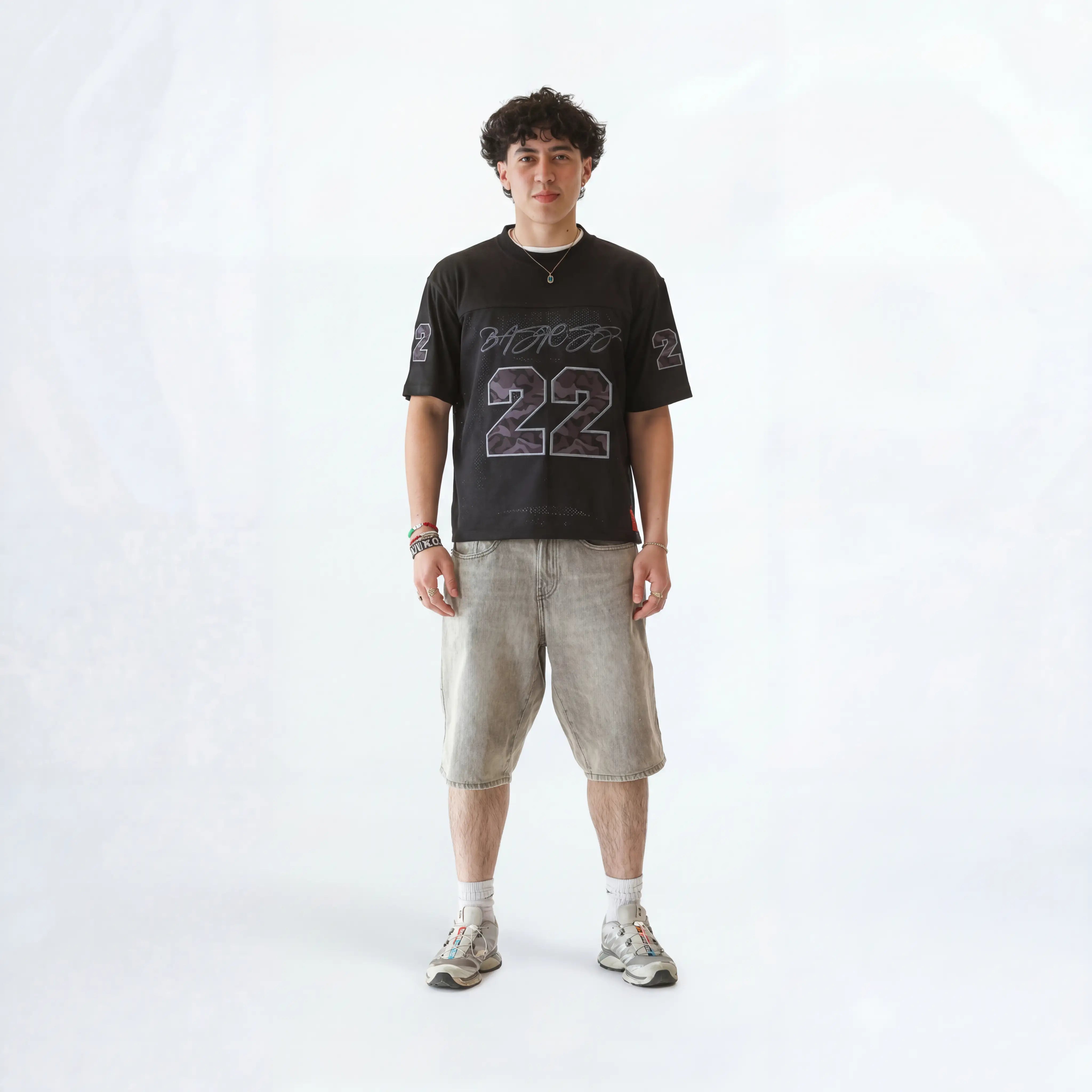 Person wearing a black t-shirt with text and numbers, light-colored shorts, and sneakers on a white background