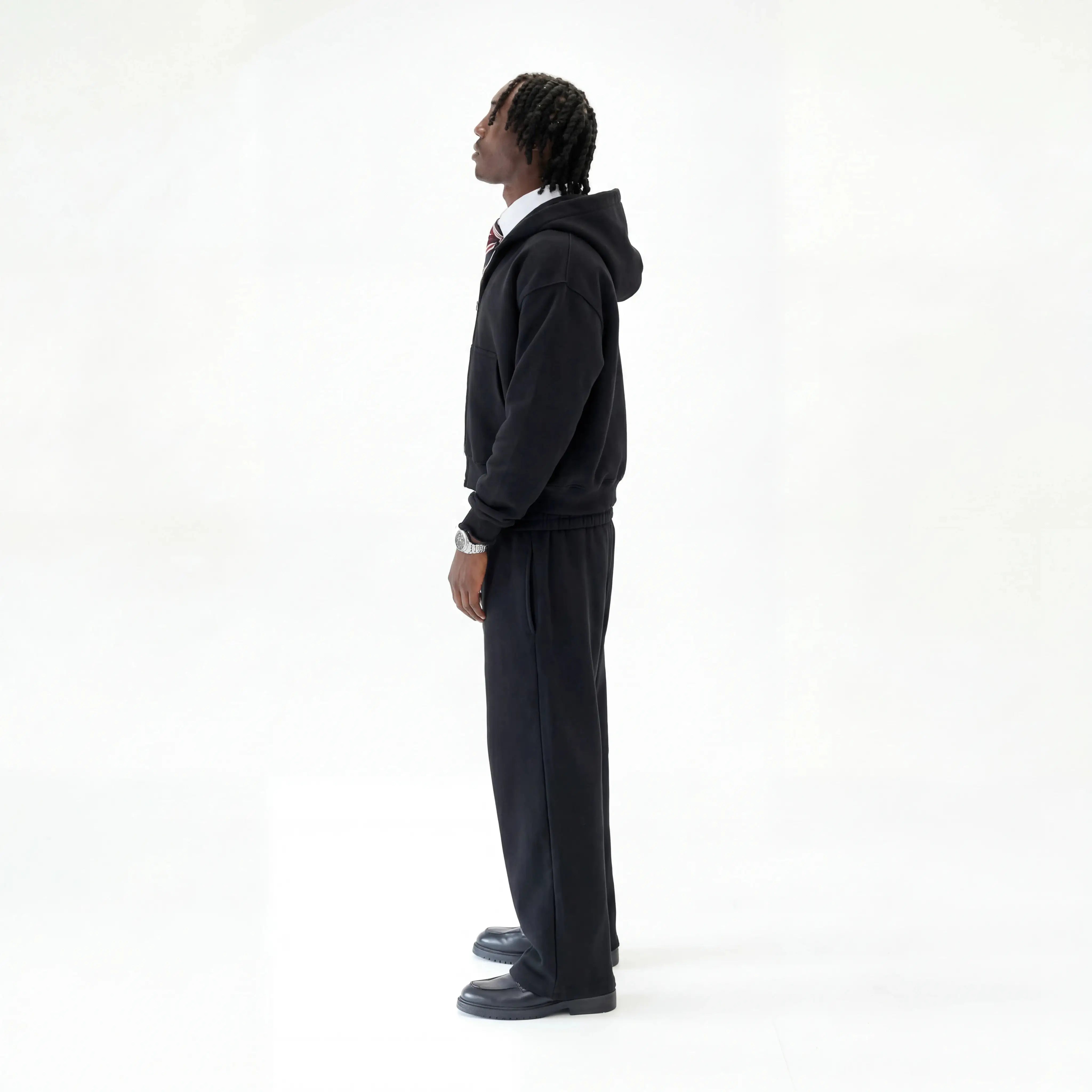 Model wearing Premium black tracksuit on white studio background facing the side. 