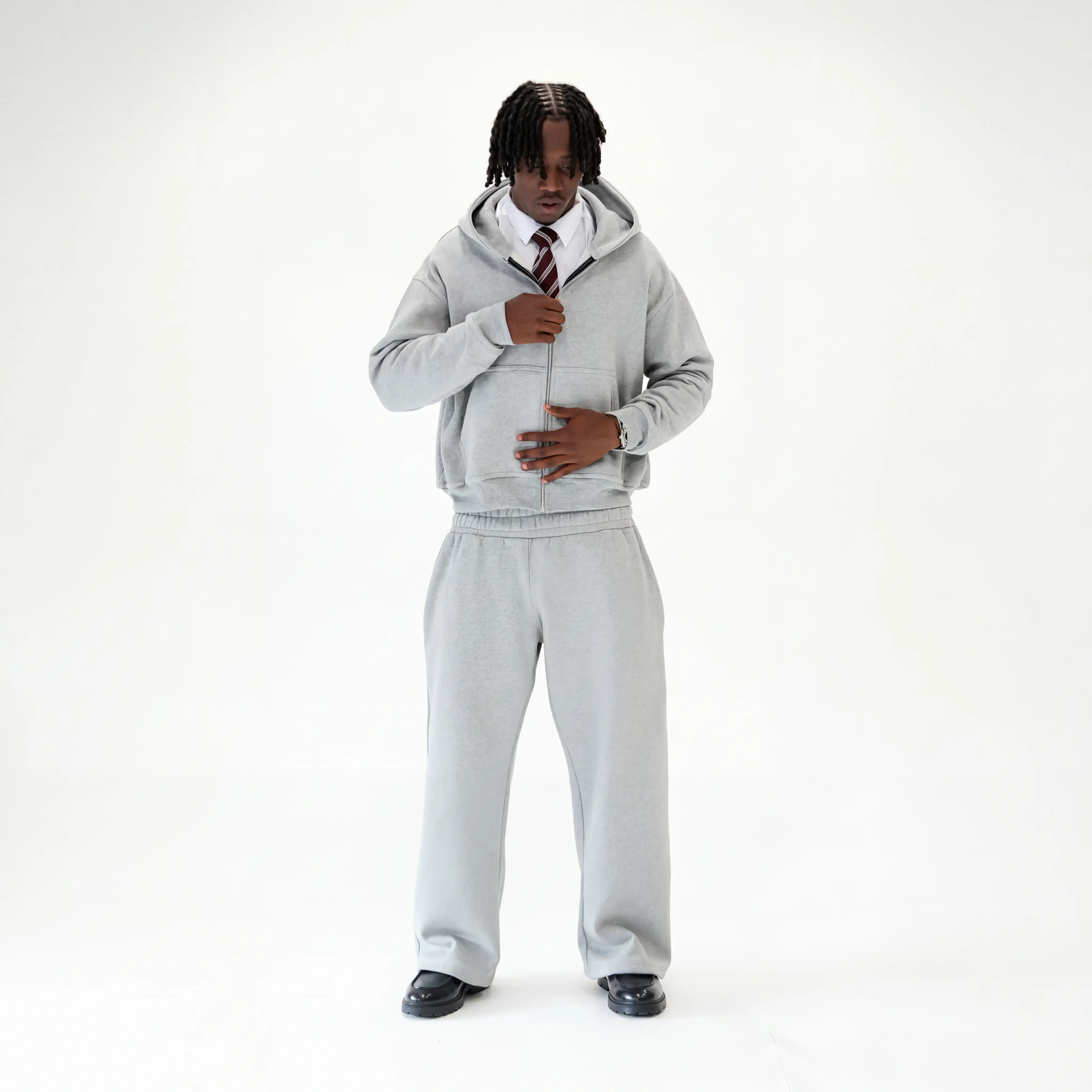 Male wearing grey tracksuit with shirt ans tie with black loafers on a white studio background