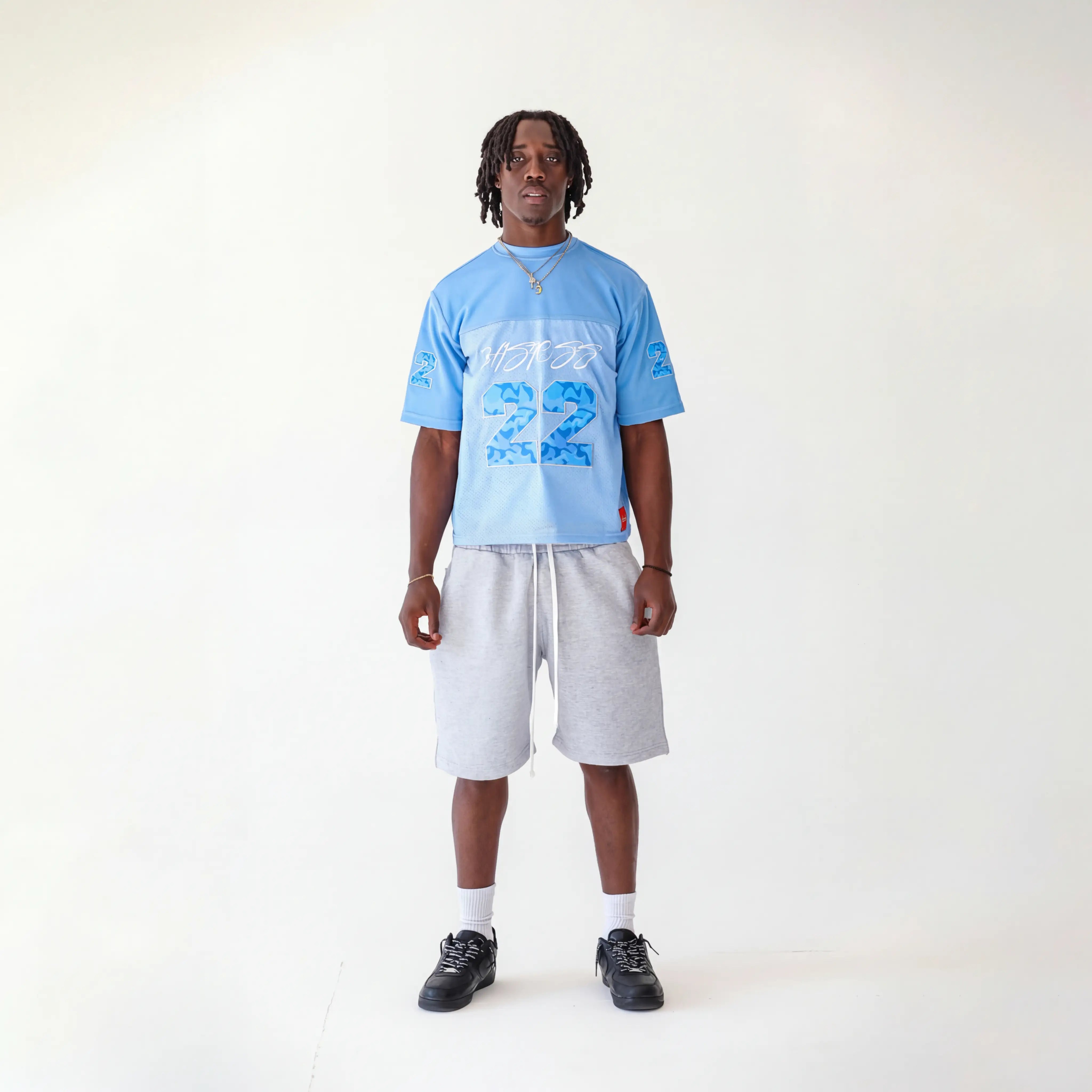 Person wearing a light blue jersey with text and numbers, white shorts, and black shoes on a white background